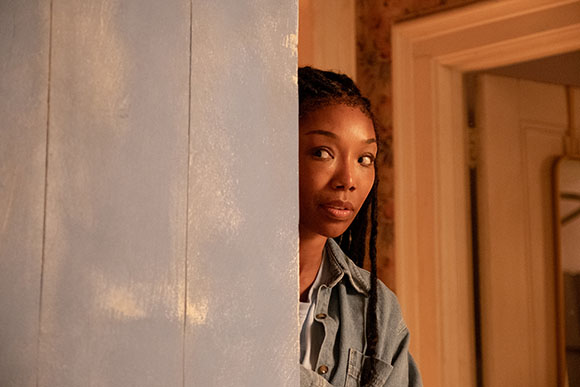 A woman with braided hair peeks from behind a light blue wooden wall.