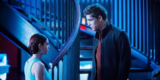 A young man in a dark jacket looks down at a young woman in a light blue top near a blue-lit staircase.