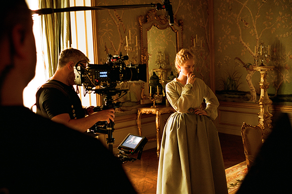 A camera operator films an actress in a long gown within an ornate, classical room.