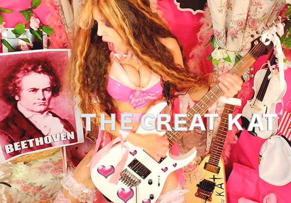 A person in pink lingerie holds a white electric guitar in front of a portrait of Beethoven.