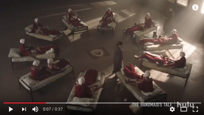 Several people in red robes lie on individual beds arranged in a large circle around a central space.