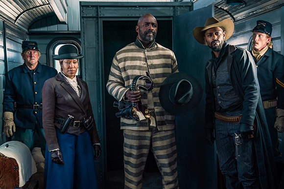 Five people in historical costumes stand inside a vintage-style train car.