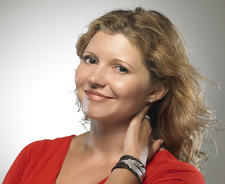 A smiling woman with blonde wavy hair wearing a red top and a black wristband.