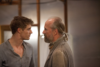 A young man with brown hair looks intensely at an older man with a grey beard in profile.