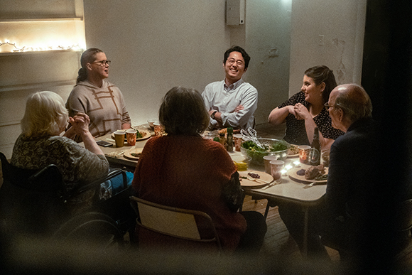 A group of diverse people sitting around a dining table, talking and laughing during a meal.