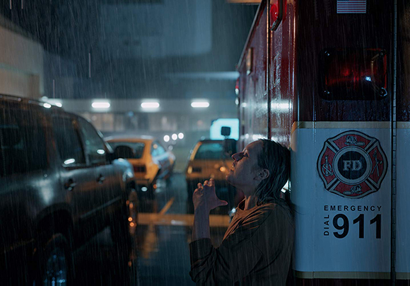 A person leans their head against a red emergency vehicle on a dark, rainy street at night.