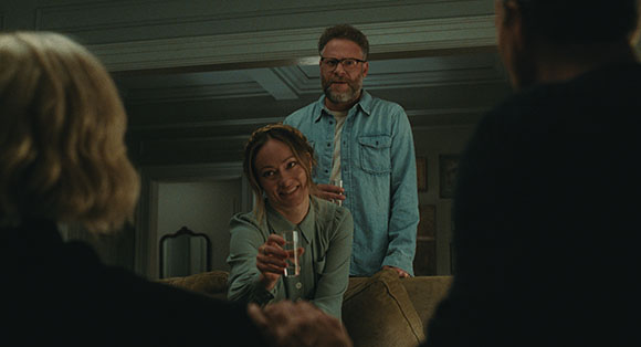 A woman smiles while holding a shot glass, with a man in a denim shirt standing behind her.