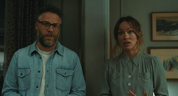 A man with glasses and a beard and a woman with blonde hair look toward the camera with surprised expressions.