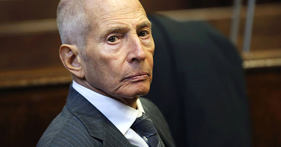 Close-up portrait of an elderly man with a serious expression wearing a dark pinstripe suit and white shirt.
