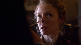 A woman looks upward while a medical instrument is applied to her nose in a dimly lit setting.