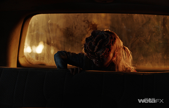 A creature with a textured, brain-like head and long hair peers through a rear car window.