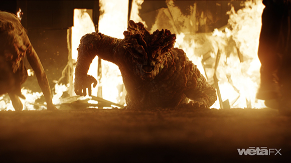 A large, bumpy-skinned creature crawls through bright flames and debris.