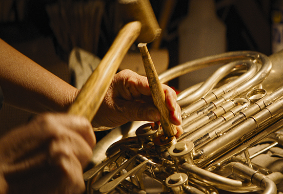 A person uses a wooden mallet to adjust the valves of a large brass instrument.