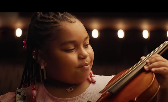 A young girl with braided hair looks down while playing a violin.