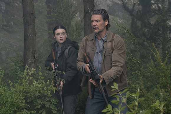 A man and a woman stand in a misty forest, both holding rifles and looking alert.