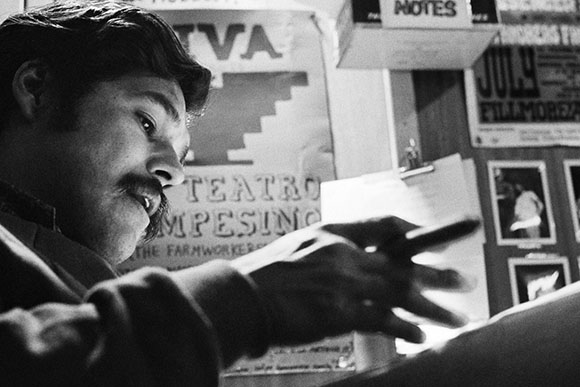 Black and white close-up of a man with a mustache looking down while holding a pen.