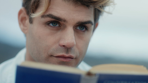 Close-up of a man with blonde hair looking down while reading a blue book.