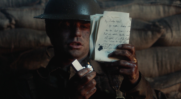 A soldier in a helmet holds a small handwritten note and a lighter in a dark, outdoor setting.
