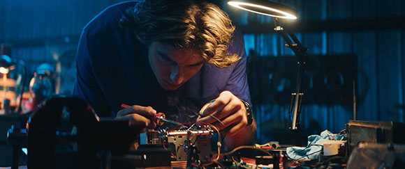 A person focused on repairing electronic components using a screwdriver under a bright desk lamp.