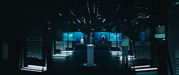 A person stands in a dark room filled with glowing blue digital displays and text panels.