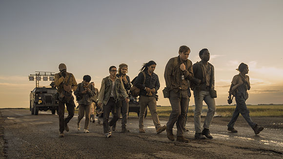 A group of people in worn clothing walking down a road toward the camera during sunset.