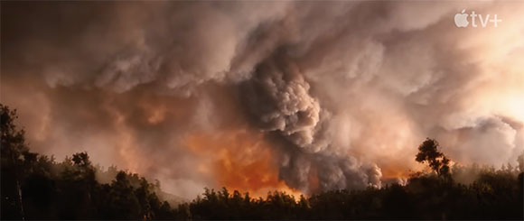 Large, billowing clouds of dark and orange smoke rising above a dark forest line.