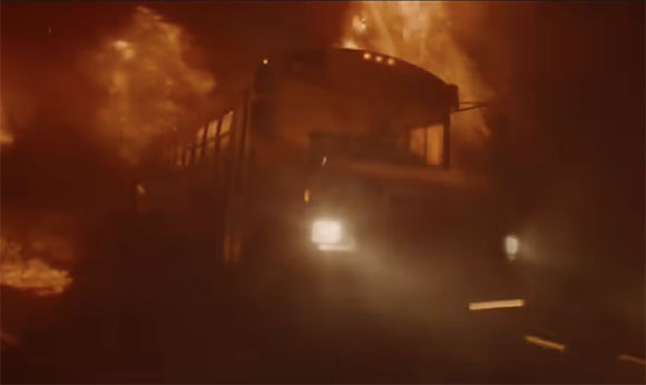 A dark train moving through heavy orange smoke and glowing firelight.