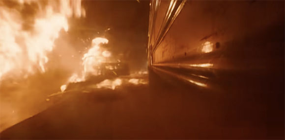 Large orange flames and thick smoke rising next to a dark, metallic structure at night.
