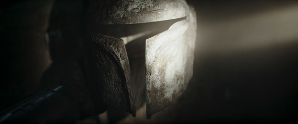 A close-up shot of a weathered, T-shaped visor helmet illuminated by a single light source.