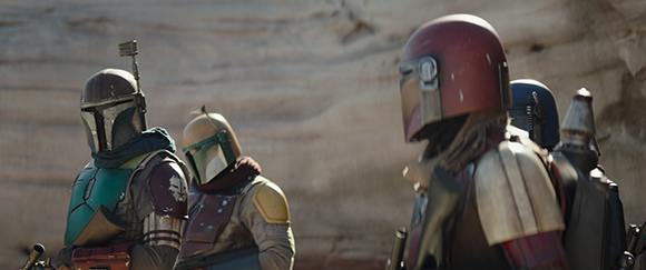 Three figures wearing Mandalorian-style helmets and armor stand in a desert setting.