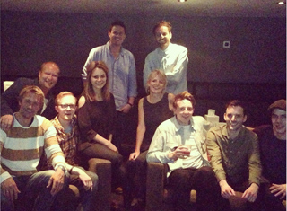 A group of ten diverse people smiling and posing together in a dimly lit indoor setting.