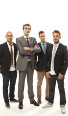 Four men standing in a group, wearing various suits, blazers, and trousers against a white backdrop.
