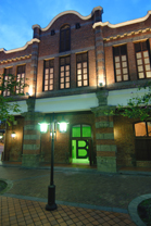 A two-story brick building with lit windows and a black street lamp in the foreground at dusk.