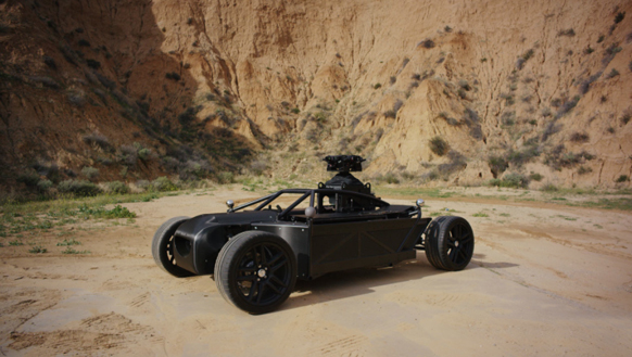A black, open-frame off-road vehicle parked on a sandy path in a desert canyon.