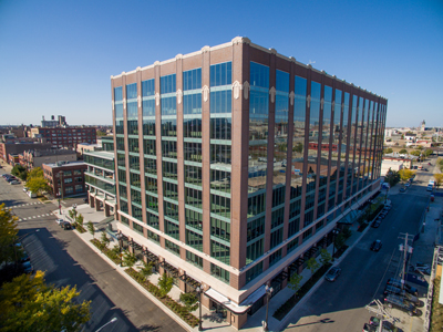 Aerial view of a large multi-story brick building with glass windows on a city street corner.