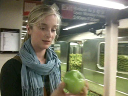 A woman with blonde hair wearing a light blue scarf holds a green apple.