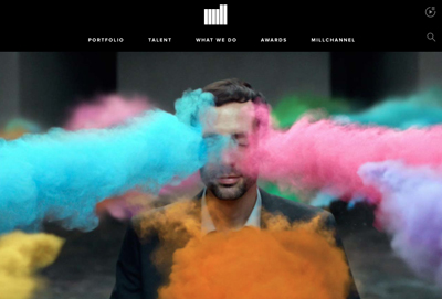 A man in a suit is partially covered by vibrant clouds of blue, pink, and orange smoke.