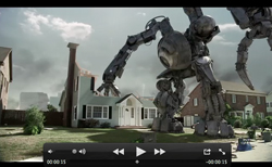 A massive metallic robot strides through a suburban street past houses and lawns under a cloudy sky.