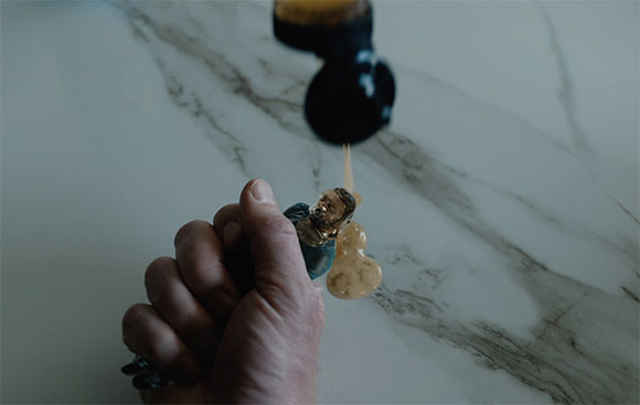 A person's hand holds a dark bottle, pouring a light brown liquid onto a marble surface.