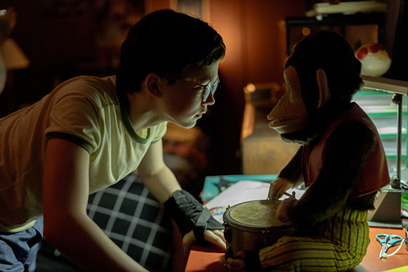 A boy in glasses leans forward to face a stuffed monkey toy sitting on a table.