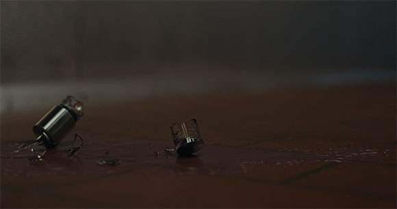 Broken glass shards and a small metal cylinder lying on a dark, reflective floor.