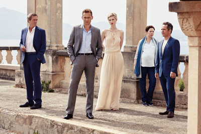 Five people in formal attire standing on a stone terrace with a body of water in the background.