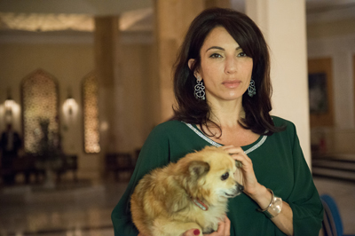 A woman in a green top holds a small tan dog in a large, dimly lit hall.