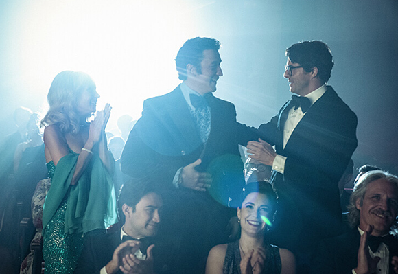 People in formal wear laughing and clapping in a dimly lit, backlit room.