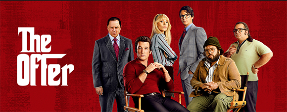 Six actors posing in various formal and casual attire against a solid red backdrop.