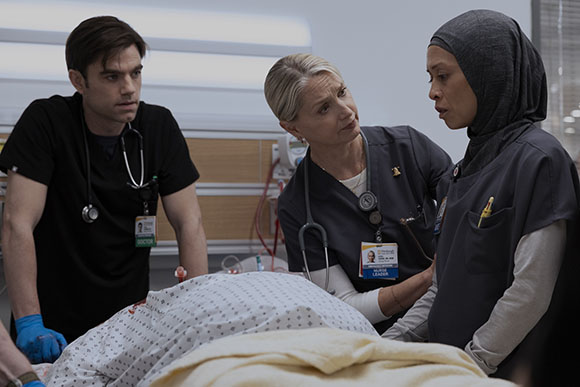 Three medical staff members lean over a patient lying in a hospital bed.
