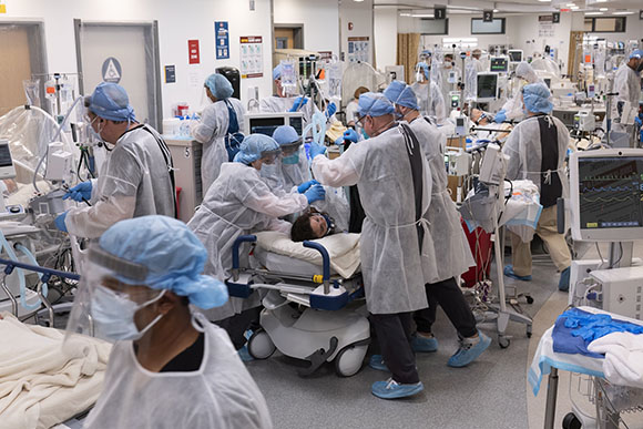 Medical professionals in protective gear attend to a patient on a gurney in a hospital ward.