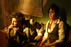 Two people with blood on their faces sit in a dark room near a map.