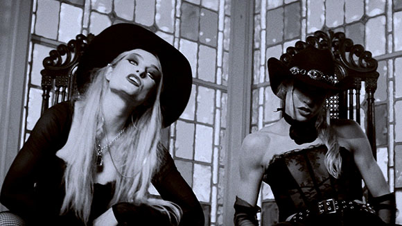 Two women in black hats and dark clothing pose in front of a large, multi-paned window.