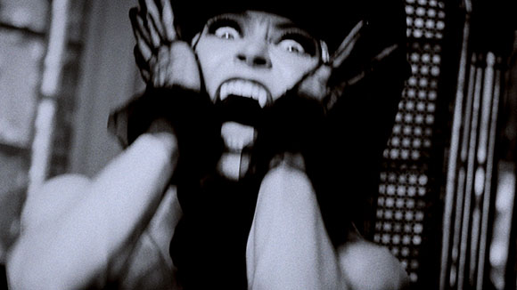 Black and white close-up of a person with wide eyes and an open mouth, expressing intense fear.